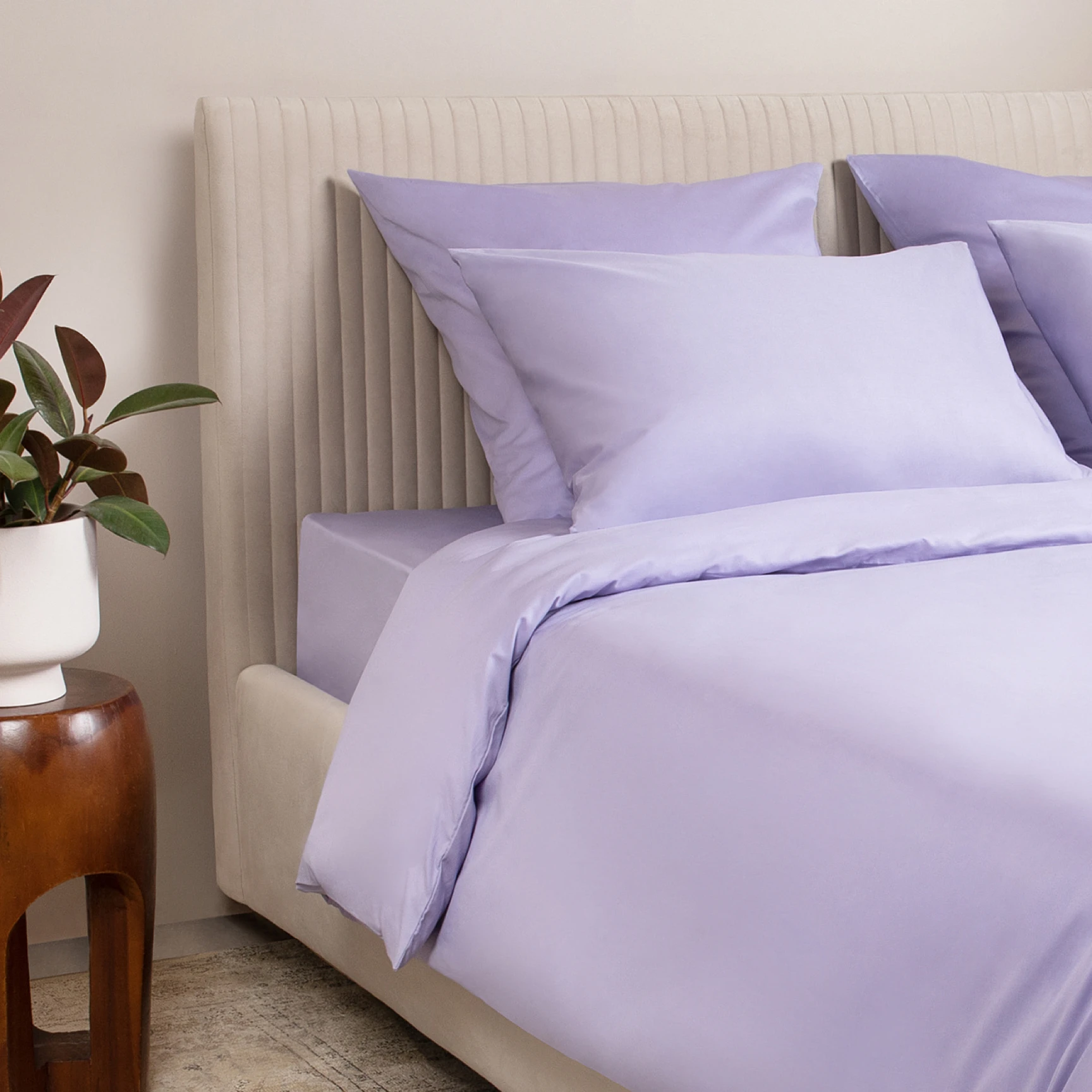 Close-up of Ecotex purple bedding. The photo demonstrates the smooth texture of the sateen fabric and pillows resting against a beige headboard